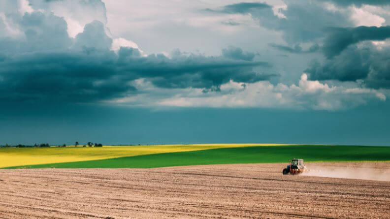 Imagen de un campo y un tractor arando con cielo nublado