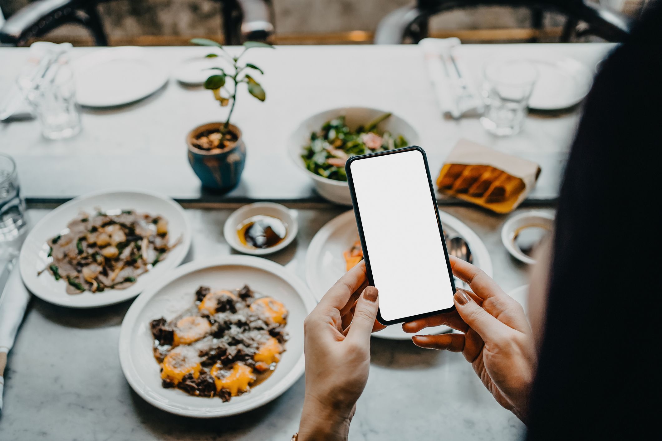 Mujer haciendo una foto con un móvil a una mesa con comida