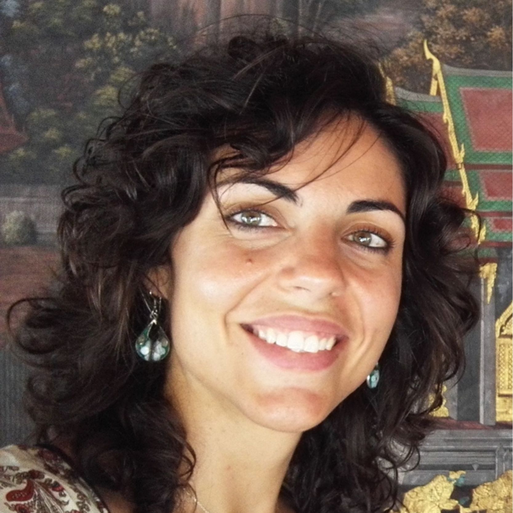 Mujer sonriente con cabello oscuro y ojos claros con pendientes.