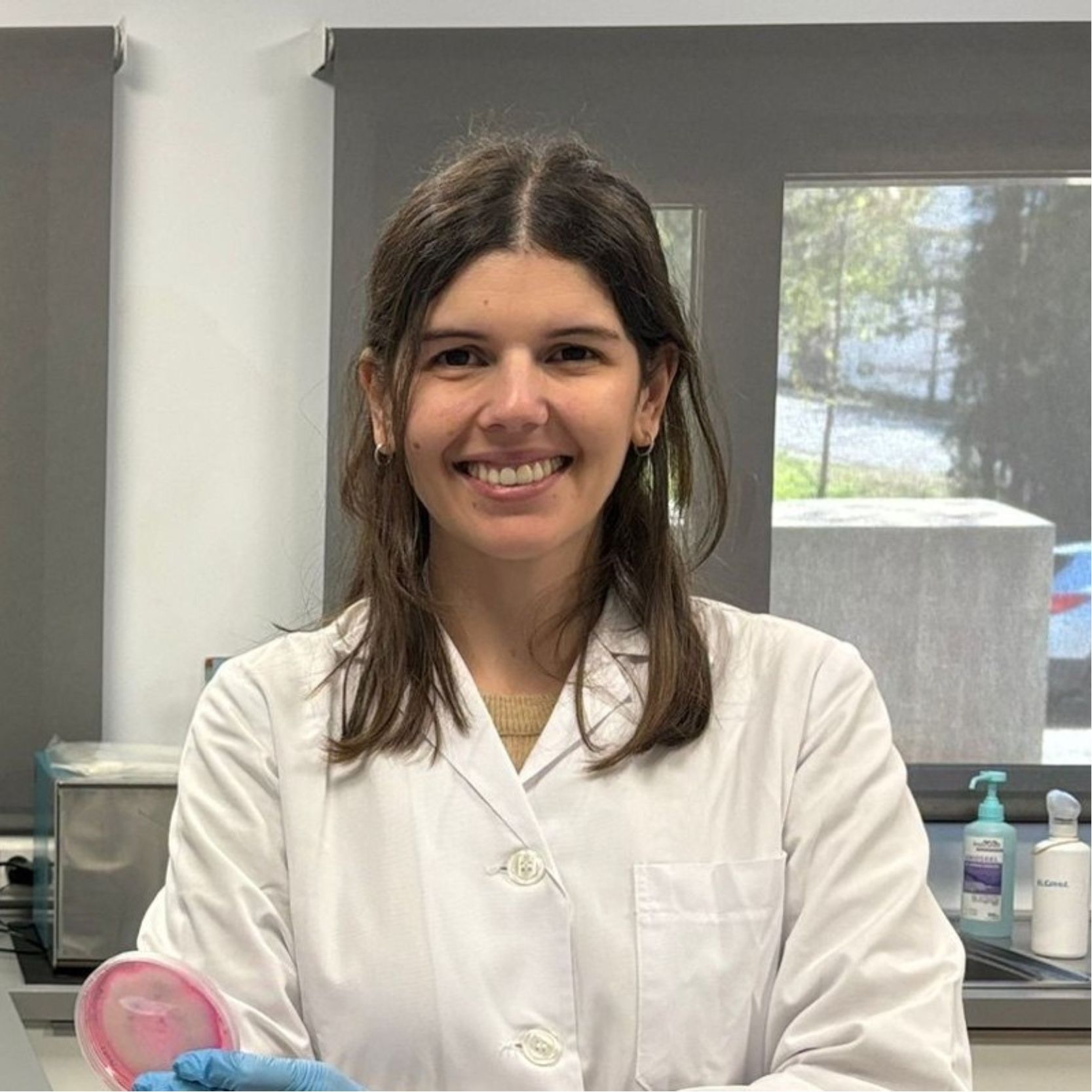 Mujer sonriente con bata de laboratorio sostiene un cultivo en un laboratorio. Mujer sonriente con bata de laboratorio sostiene un cultivo en un laboratorio.