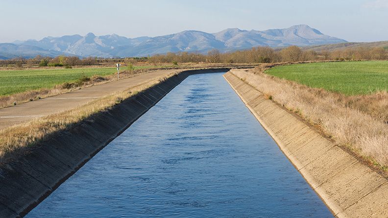 Canal de agua para el riego en paisaje con montañas al fondo