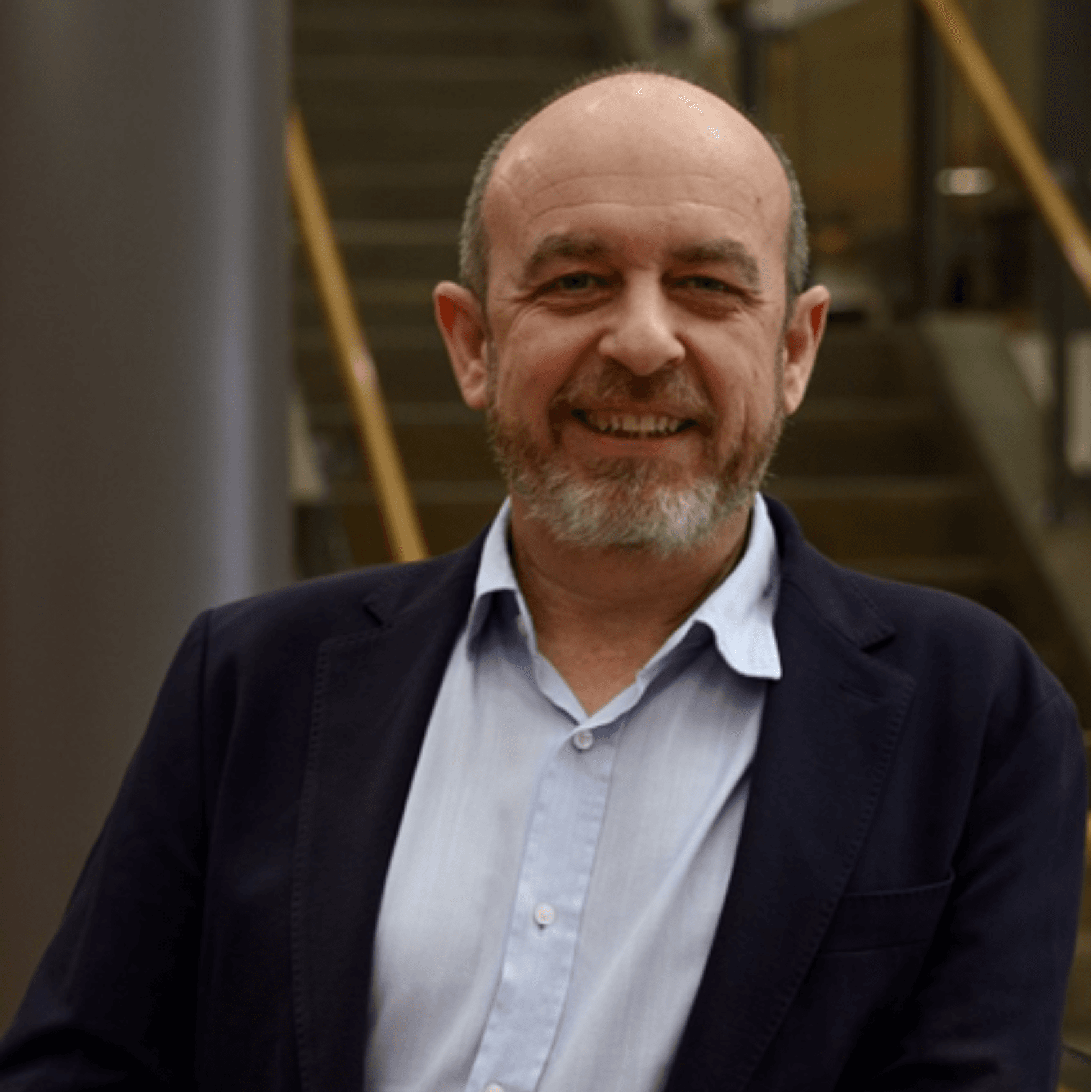 Carlos Garcés Narro Hombre sonriente con traje y camisa, en un edificio moderno.