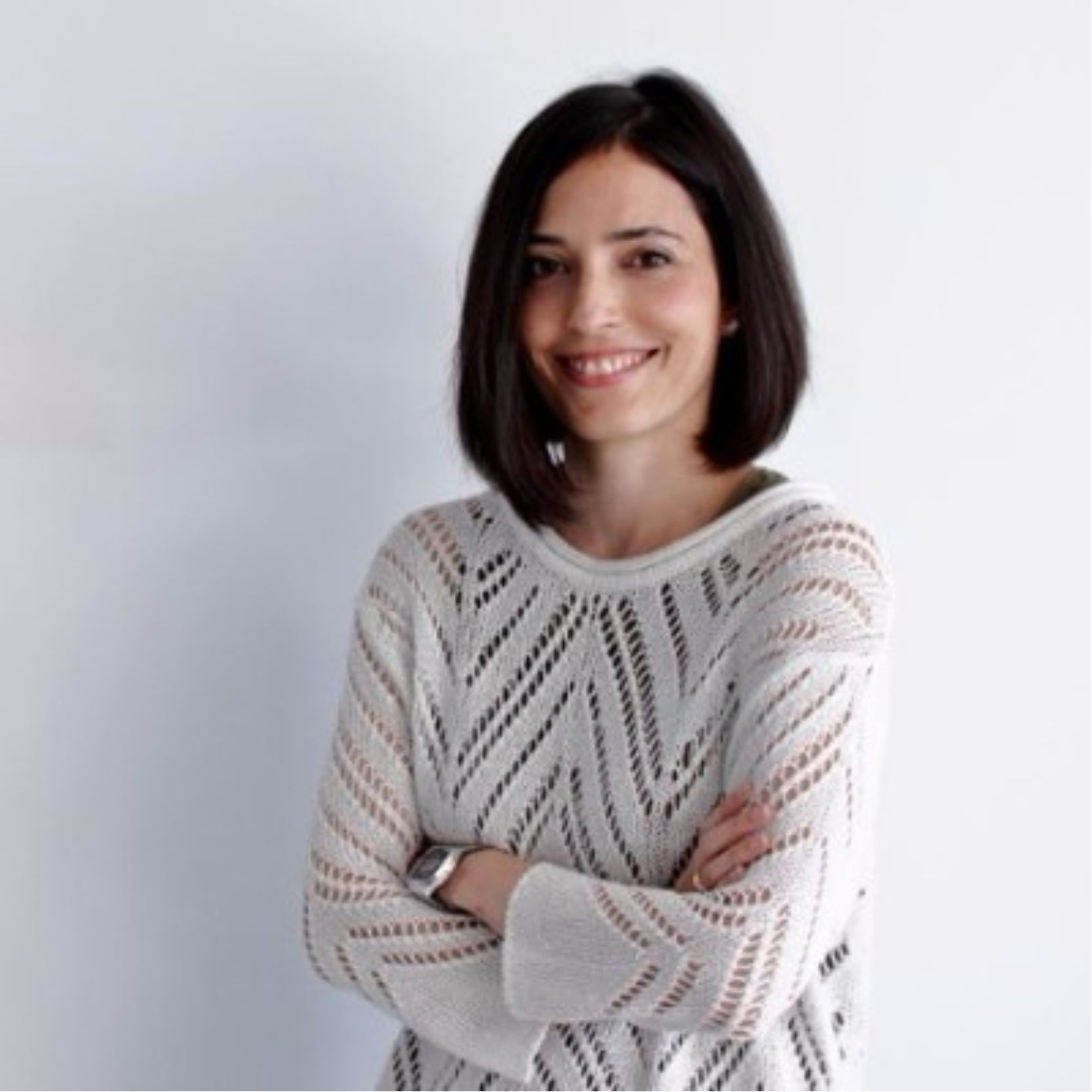 Mujer sonriente con los brazos cruzados con un suéter blanco con patrones.