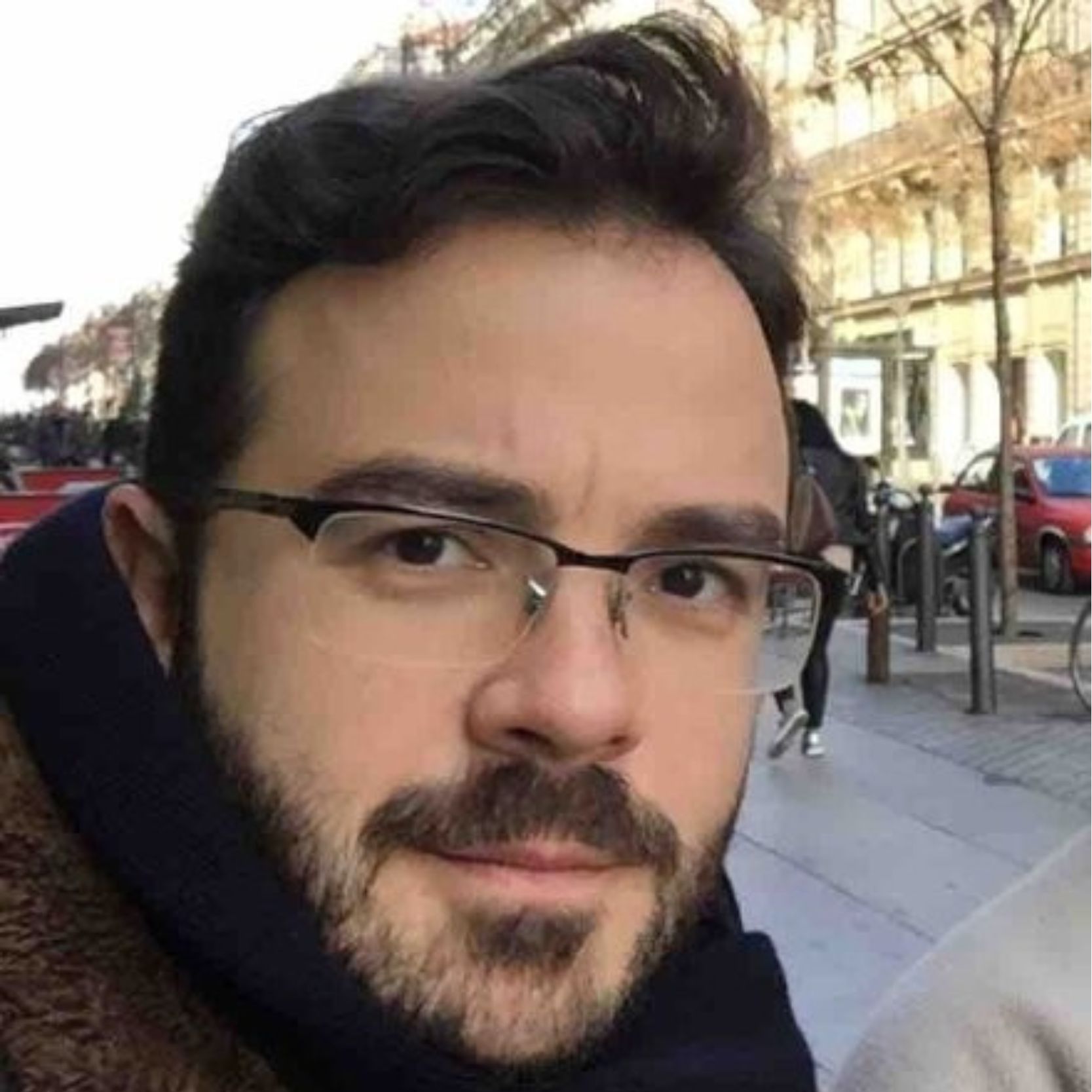 Hombre joven con bigote y gafas, en la calle.