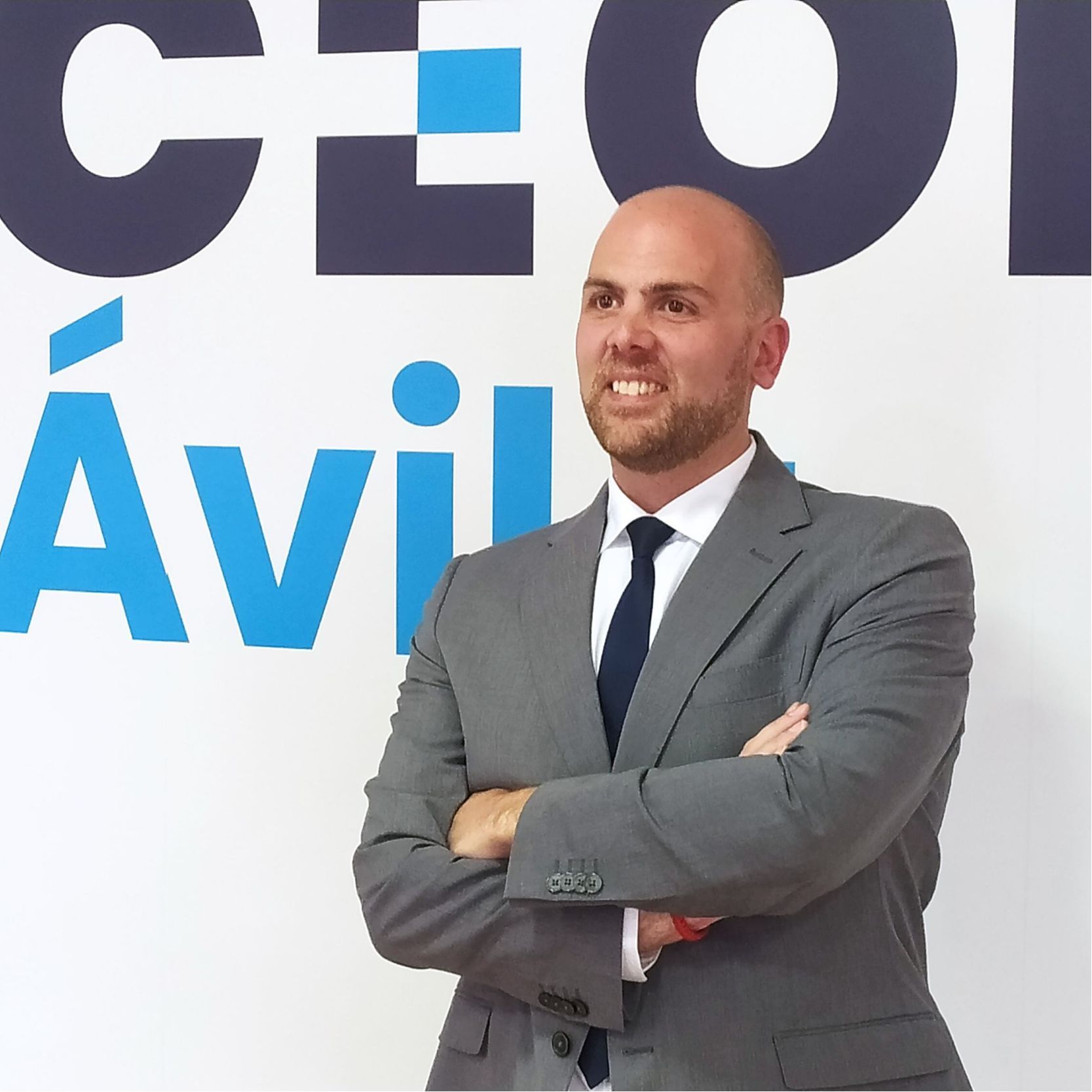 Diego Díez, con traje gris, camisa blanca y corbata oscura, brazos cruzados y sonriendo ante cartel corporativo de CEOE Ávila