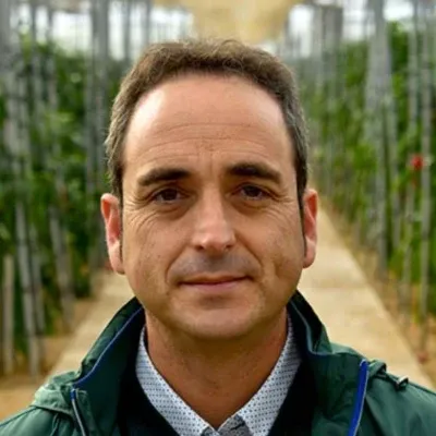 Fernando Paniagua Salvador, con chaqueta verde, posando en el interior de un invernadero con cultivos en hileras al fondo