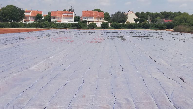 Superficie cubierta con plástico, con casas de terracota en el fondo.