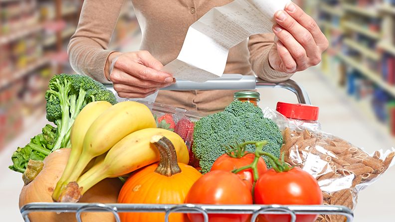 Mujer revisando el ticket de compra de su carrito con alimentos en un supermercado