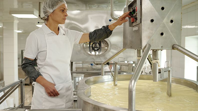Mujer en uniforme blanco monitorea la máquina de producción de queso industrial en una instalación de producción. Trabajadora que garantiza el control de calidad en el proceso de elaboración del queso