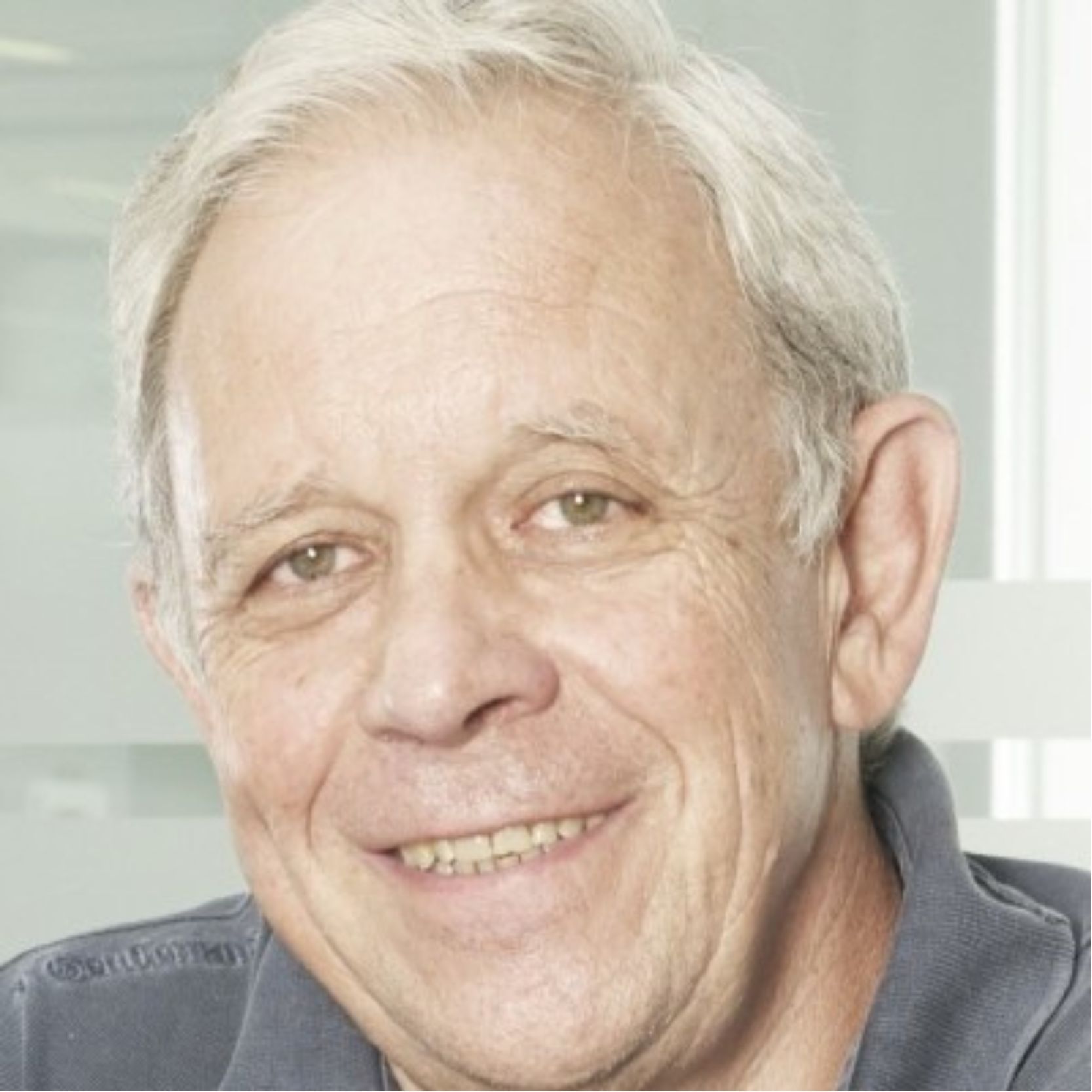 Hombre mayor sonriendo con cabello gris y ojos verdes.
