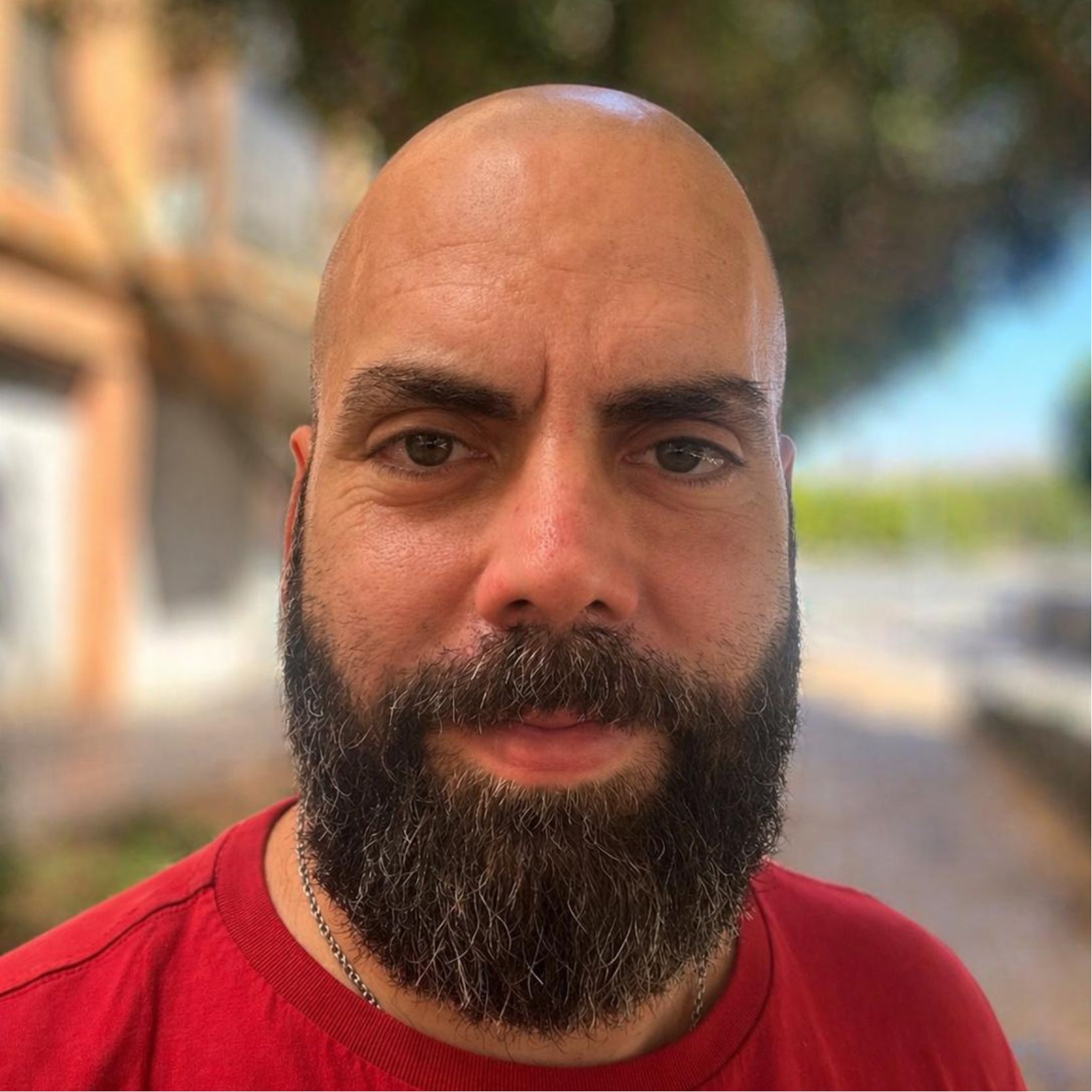 Hombre calvo con barba y bigote, usando una camiseta roja.