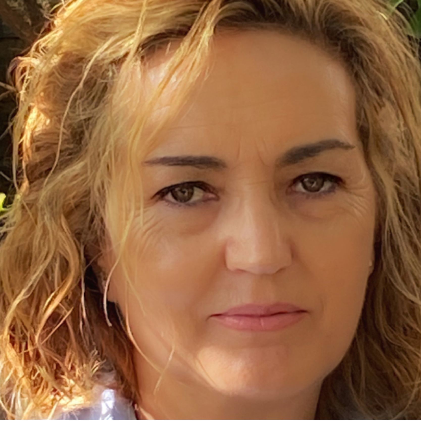 Mujer con el cabello claro y ojos marrones, mirando hacia adelante con seriedad.