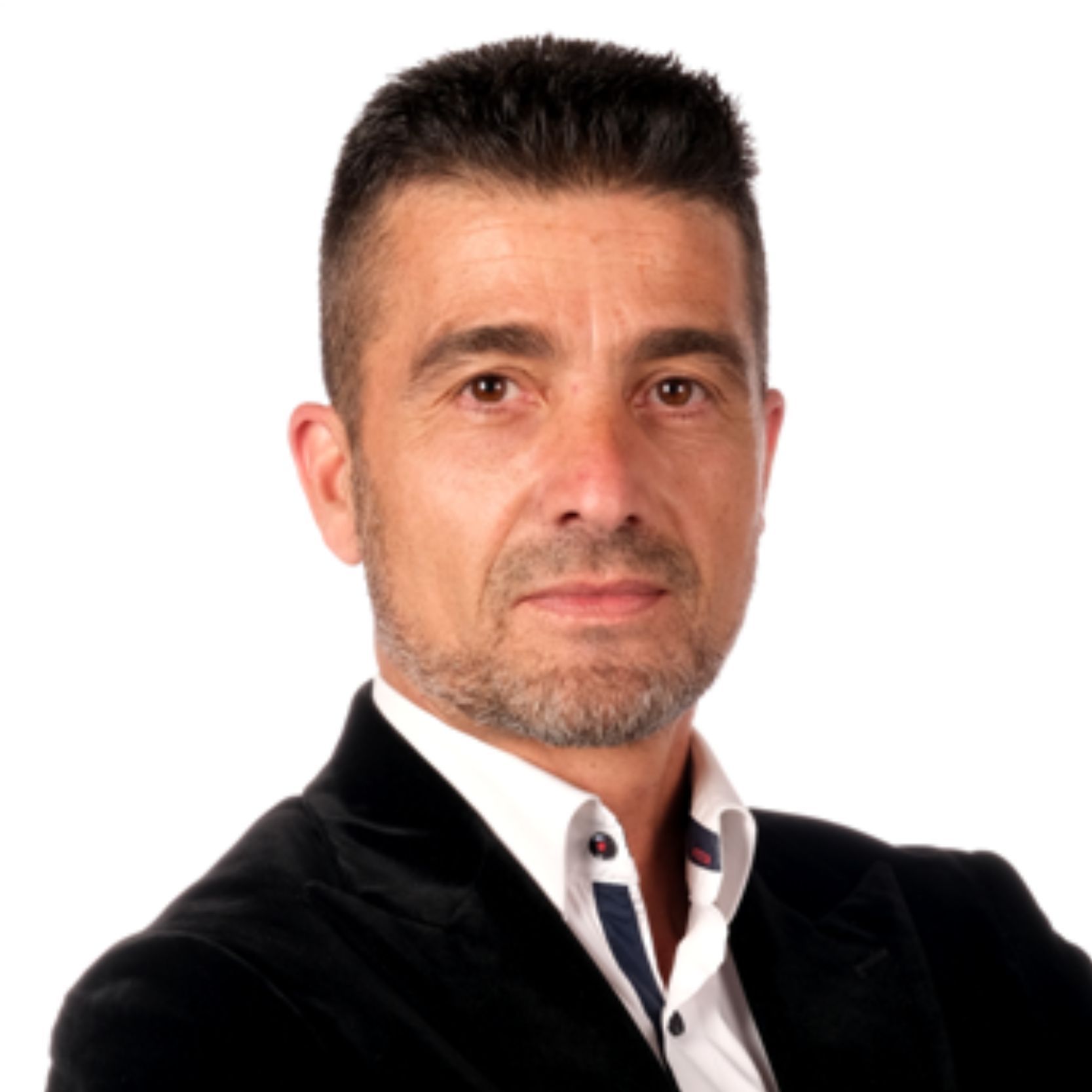 Hombre con cabello corto y barba, traje negro, fondo blanco.