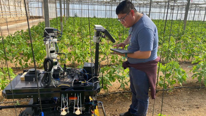 Hombre revisando un robot agrícola en un invernadero de plantas.