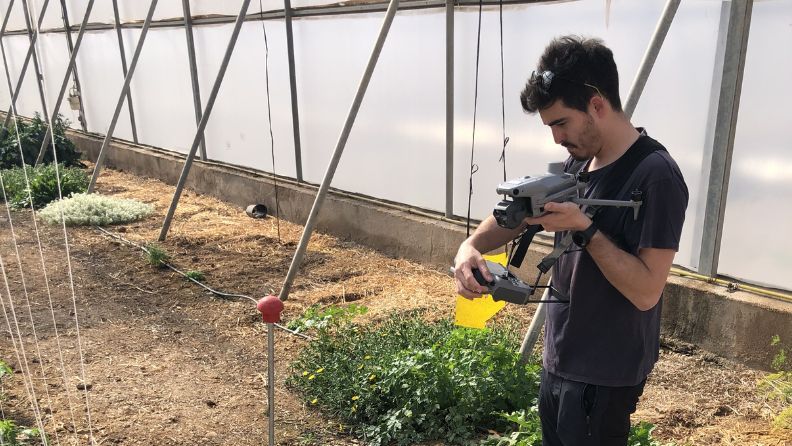 Hombre utilizando un dron en un invernadero con plantas.