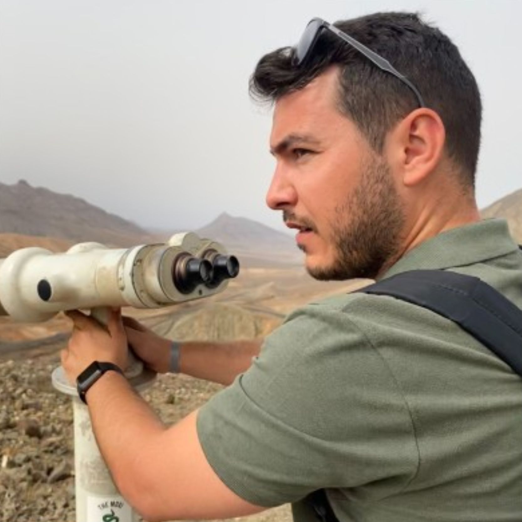Hombre usando binoculares en un paisaje montañoso.