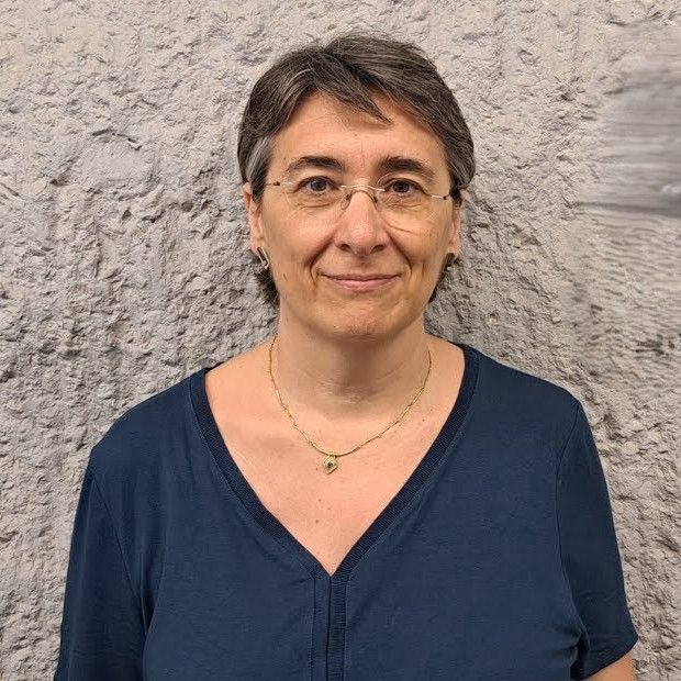 Mujer sonriente con camiseta azul y fondo de pared texturizada.