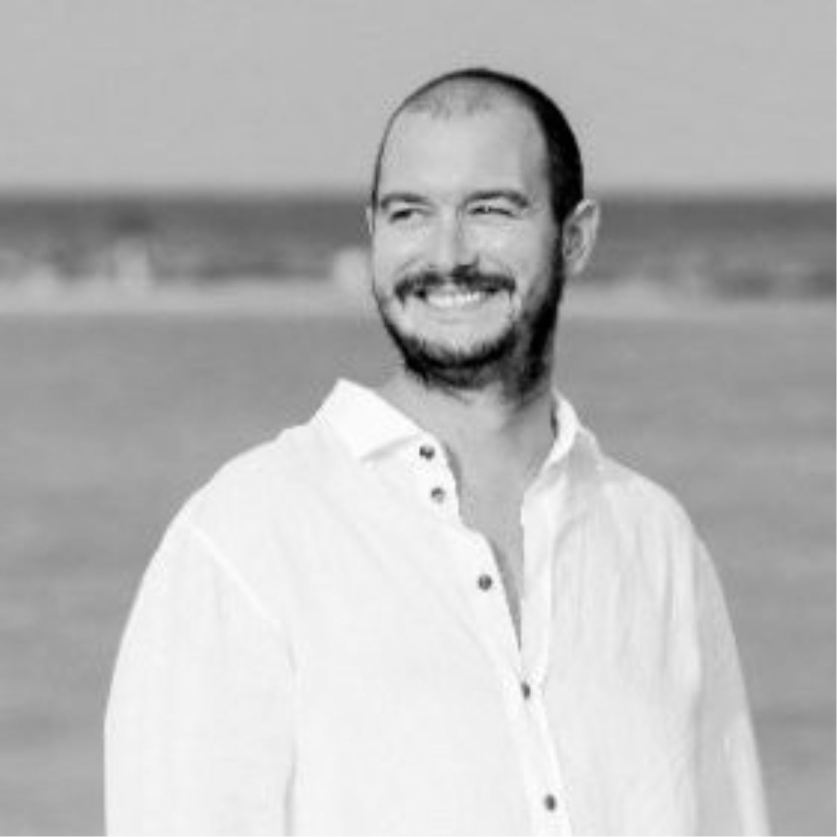 Un hombre sonriendo y con la camisa blanca en la playa.