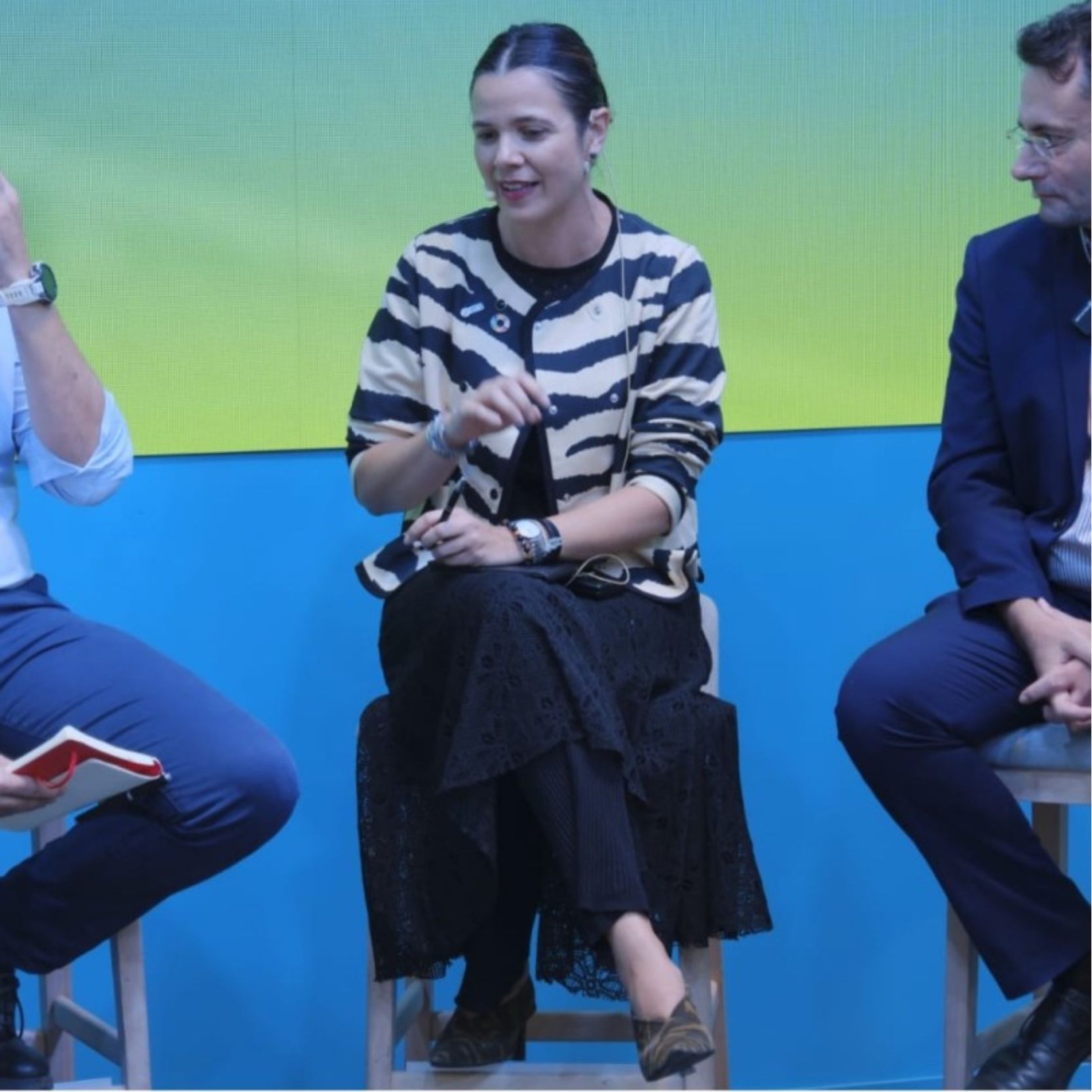 Mujer hablando en un panel con fondo azul y amarillo.