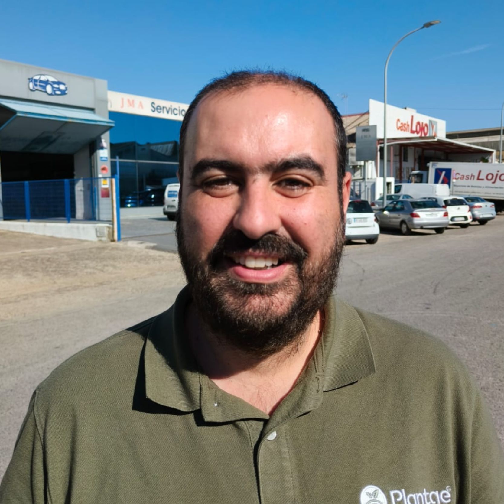 Hombre sonriendo en un estacionamiento con un polo verde.