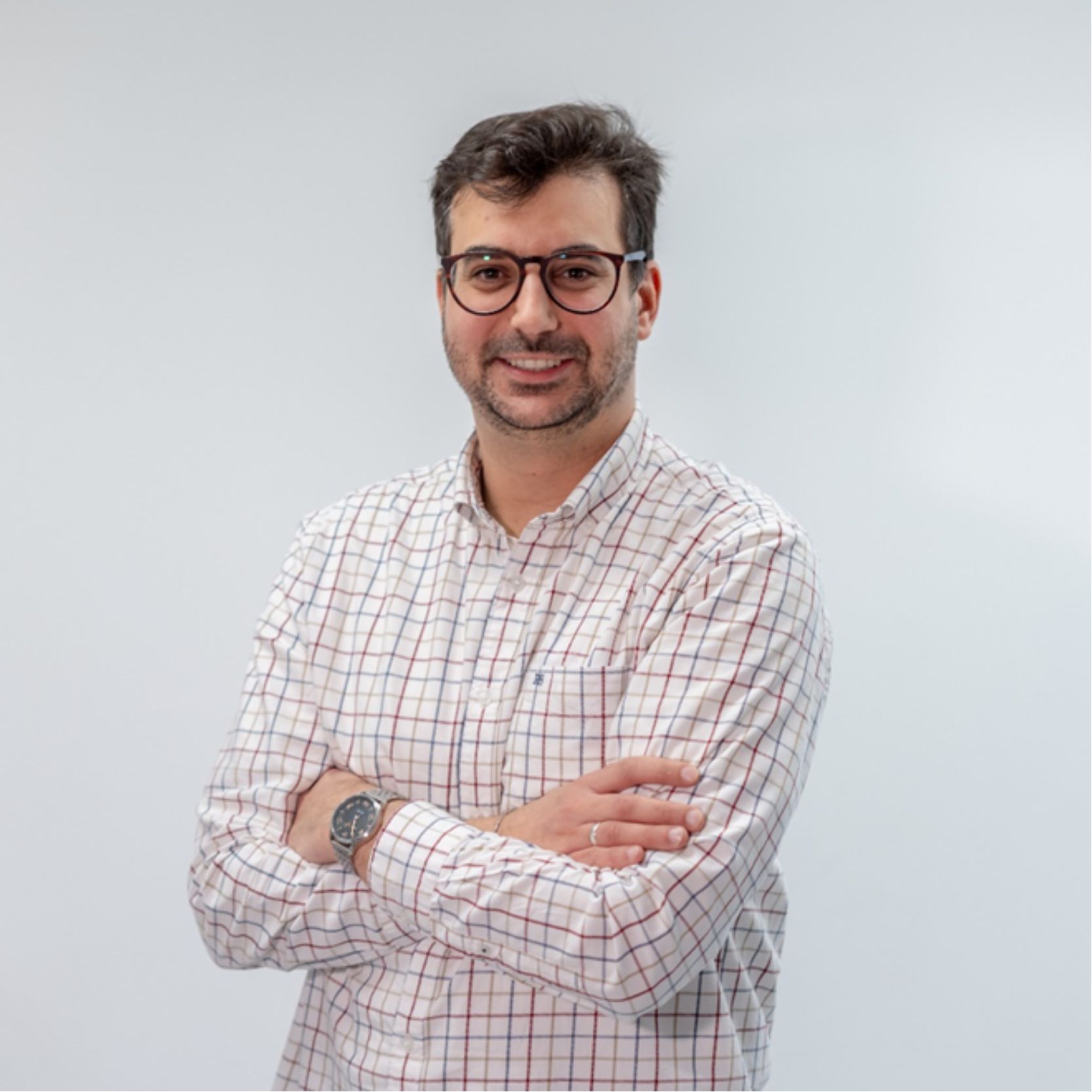 Un hombre sonriente con gafas y camisa de cuadros, con los brazos cruzados.