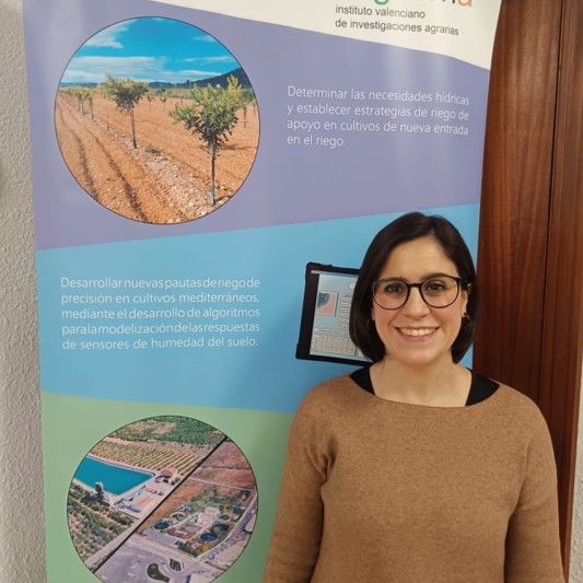 Mujer joven con gafas sonriendo cerca de un cartel de ciencia agrícola.