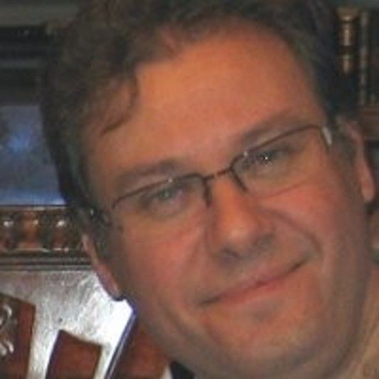Retrato de hombre con gafas sonriendo.