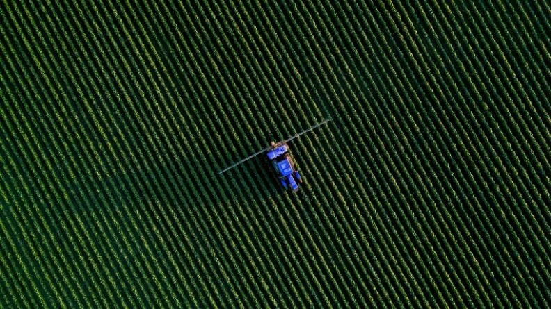 Vista de pájaro de un cultivo al aire libre con un tractor en el centro, sistema agroalimentario mundial