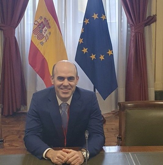 Hombre en traje sentado con banderas de España y la UE detrás.