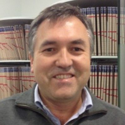 Un hombre sonriendo en una biblioteca o archivo con libros en estanterías detrás de él. Un hombre sonriendo en una biblioteca o archivo con libros en estanterías detrás de él.