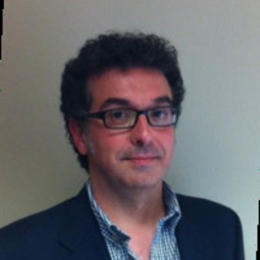 Hombre con gafas y traje, sonriendo ligeramente.