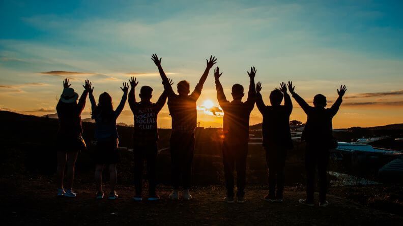 Grupo de personas con los brazos arriba frente a una puesta de sol, simulando una cooperativa agroalimentaria