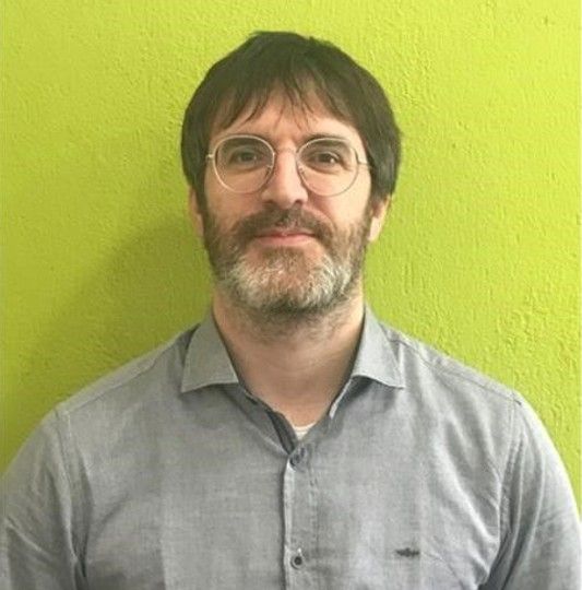 Hombre con gafas y bigote contra fondo verde.