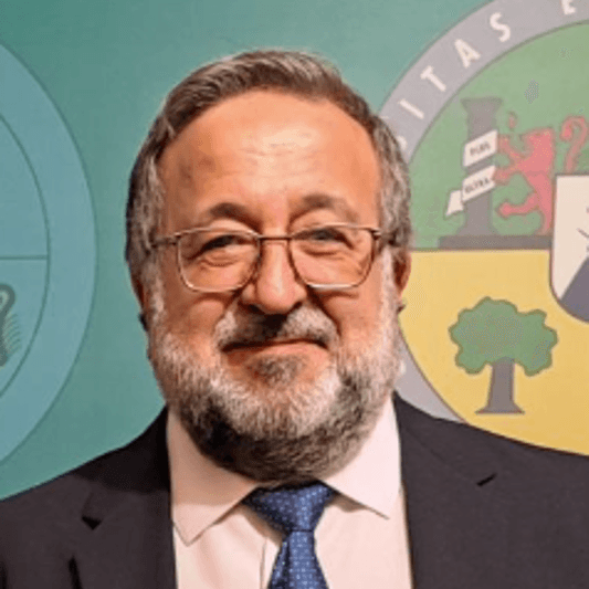 Hombre con traje y corbata, fondo con escudo y símbolos.