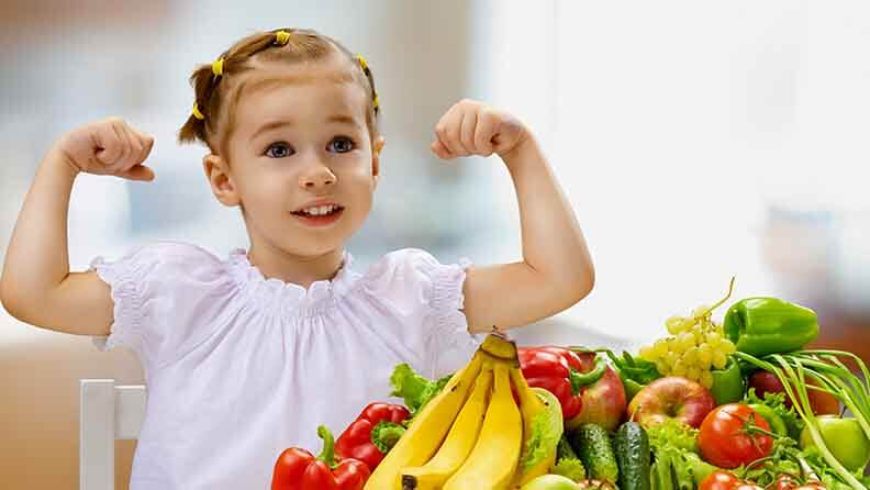 Niña rodeada de alimentos saludables como fruta y verdura