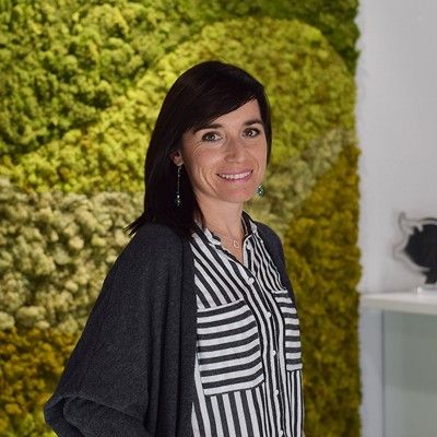 Mujer sonriendo frente a un muro verde con una blusa a rayas.