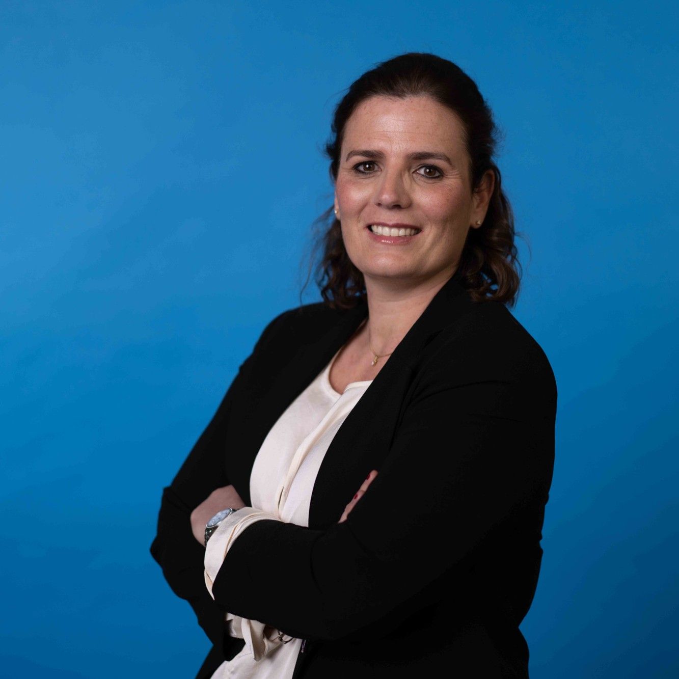 Mujer sonriente con blazer negro sobre fondo azul.