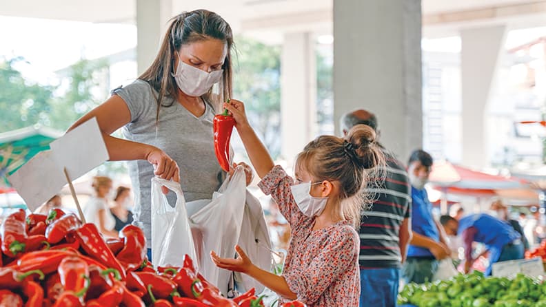 Madre e hija comprando verdura en el mercado con mascarilla