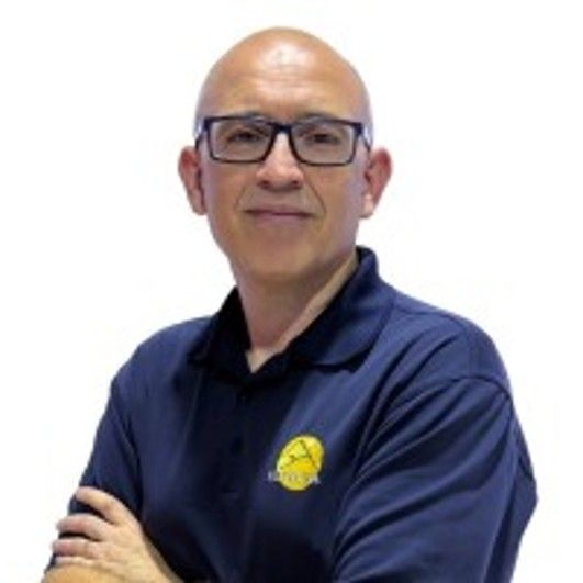 Hombre con gafas y camisa azul, brazos cruzados, sonriendo.