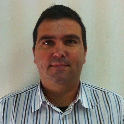 Hombre con camisa a rayas sonriendo frente a un fondo blanco.