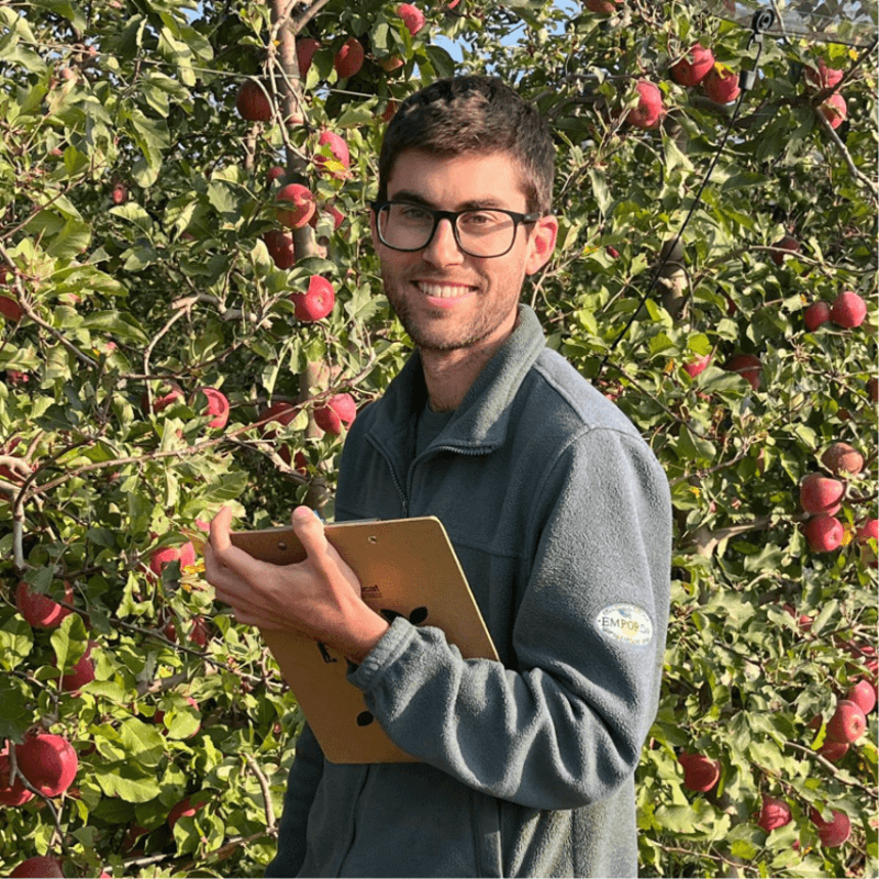 Hombre sonriendo con tableta en un campo de manzanas.