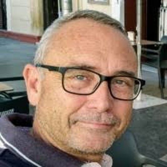 Hombre mayor con gafas y sonrisa, sentado en un restaurante.