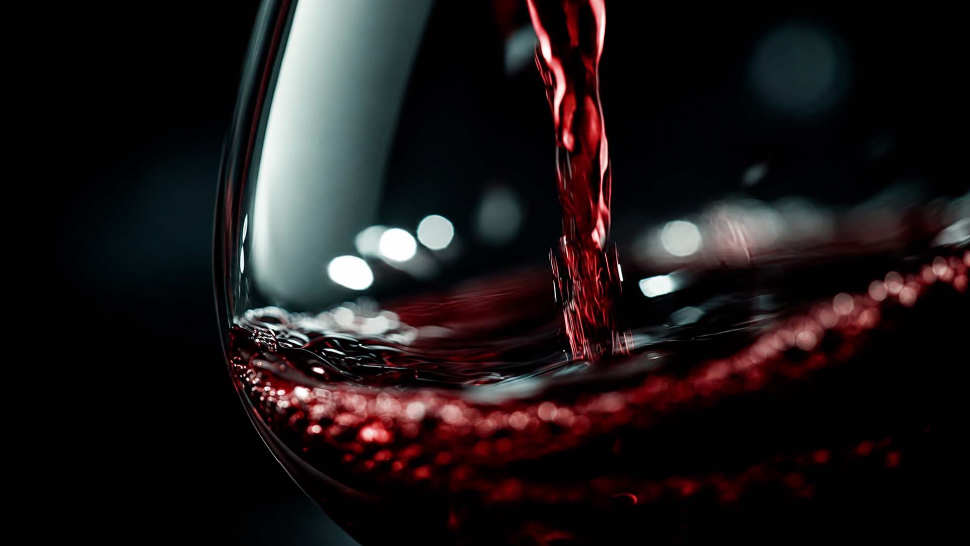 Vino tinto siendo vertido en una copa de vino, con un fondo oscuro.