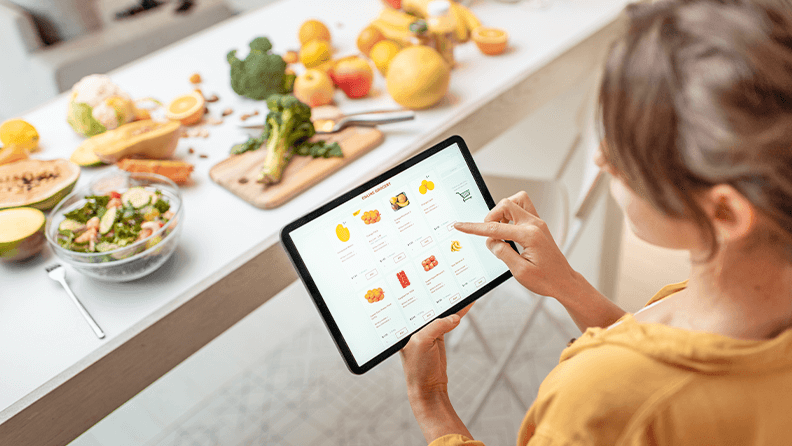 Mujer comprando comida en línea usando una tableta digital en la cocina. 