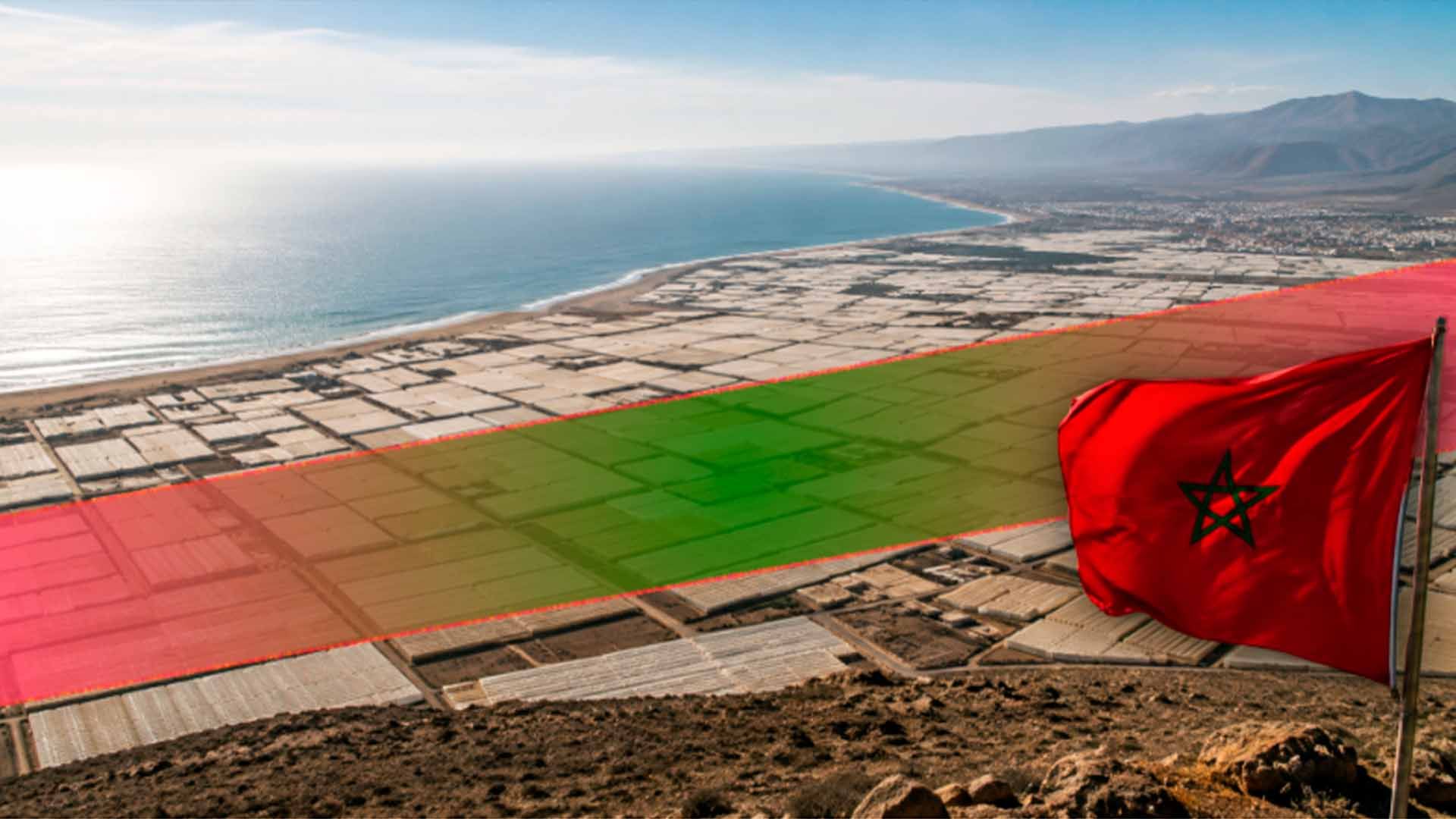 Bandera marroquí ondeando sobre costa con extensos invernaderos y franja territorial.