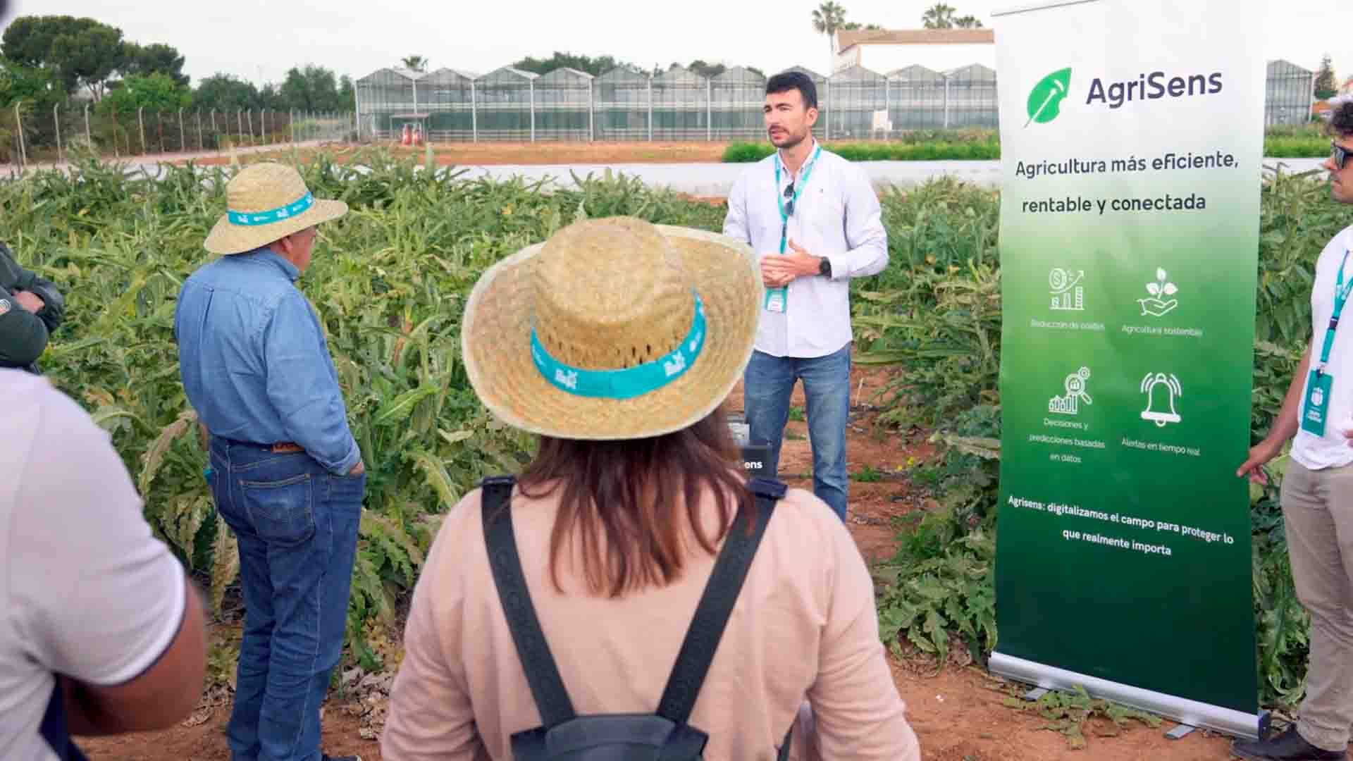 Un hombre habla en un campo de cultivo delante de un cartel de AgriSens.