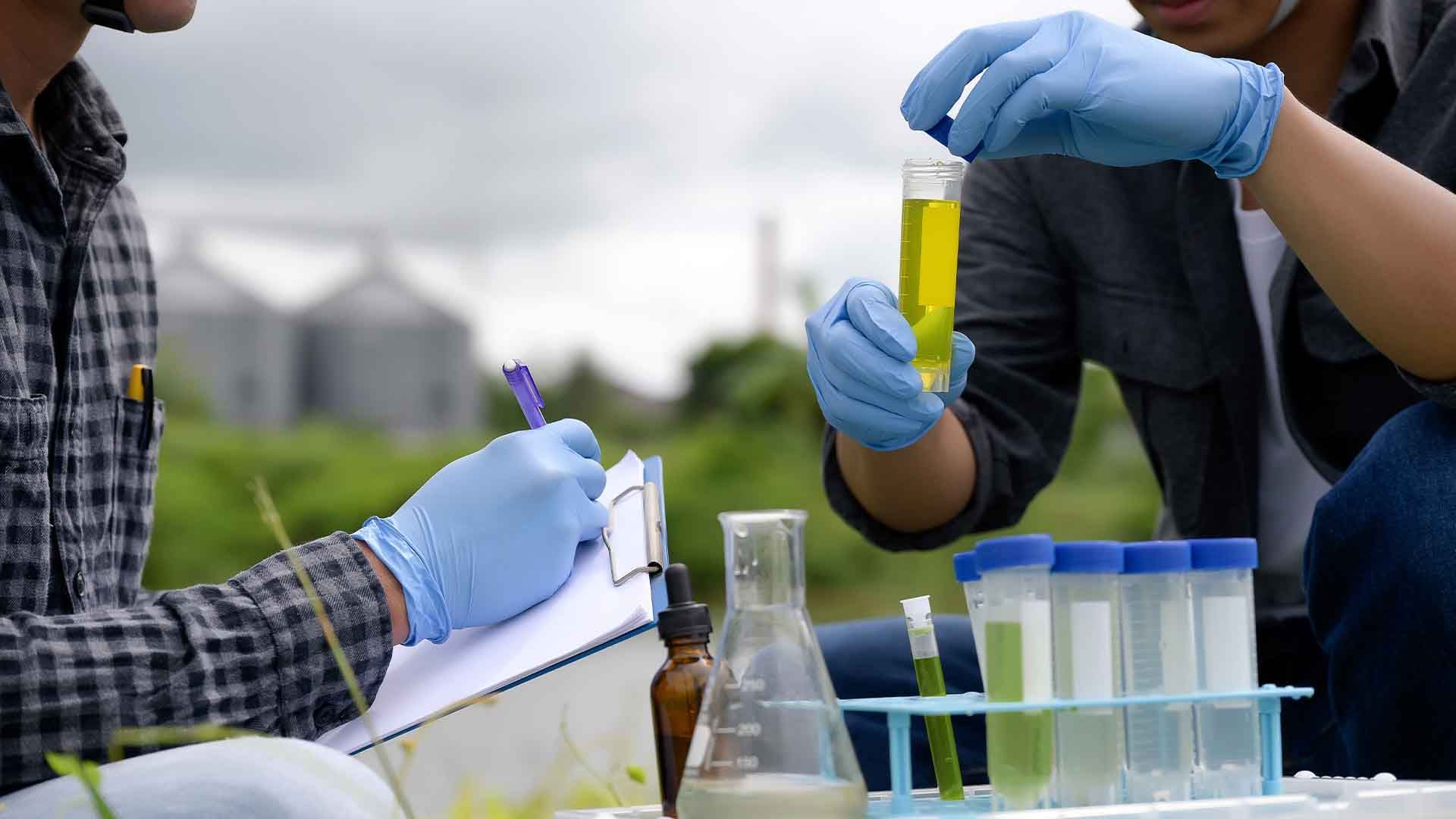 Los ingenieros ambientales inspeccionan la calidad del agua, realizan pruebas de pH y toman notas de muestras de agua en el campo, cerca de tierras de cultivo