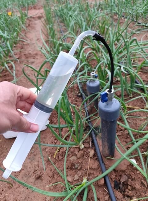 Mano sosteniendo un dispositivo de medición de fertilizante en un campo.