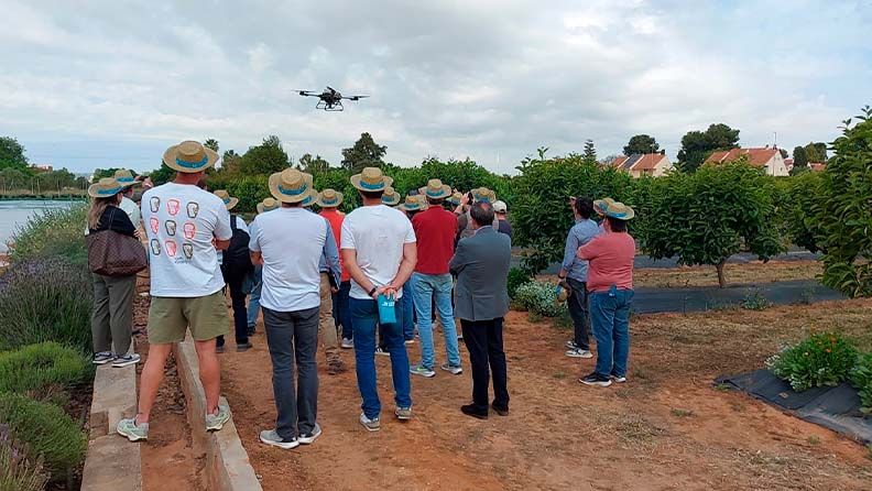 Grupo de personas observando un dron volar en un área rural o jardín.