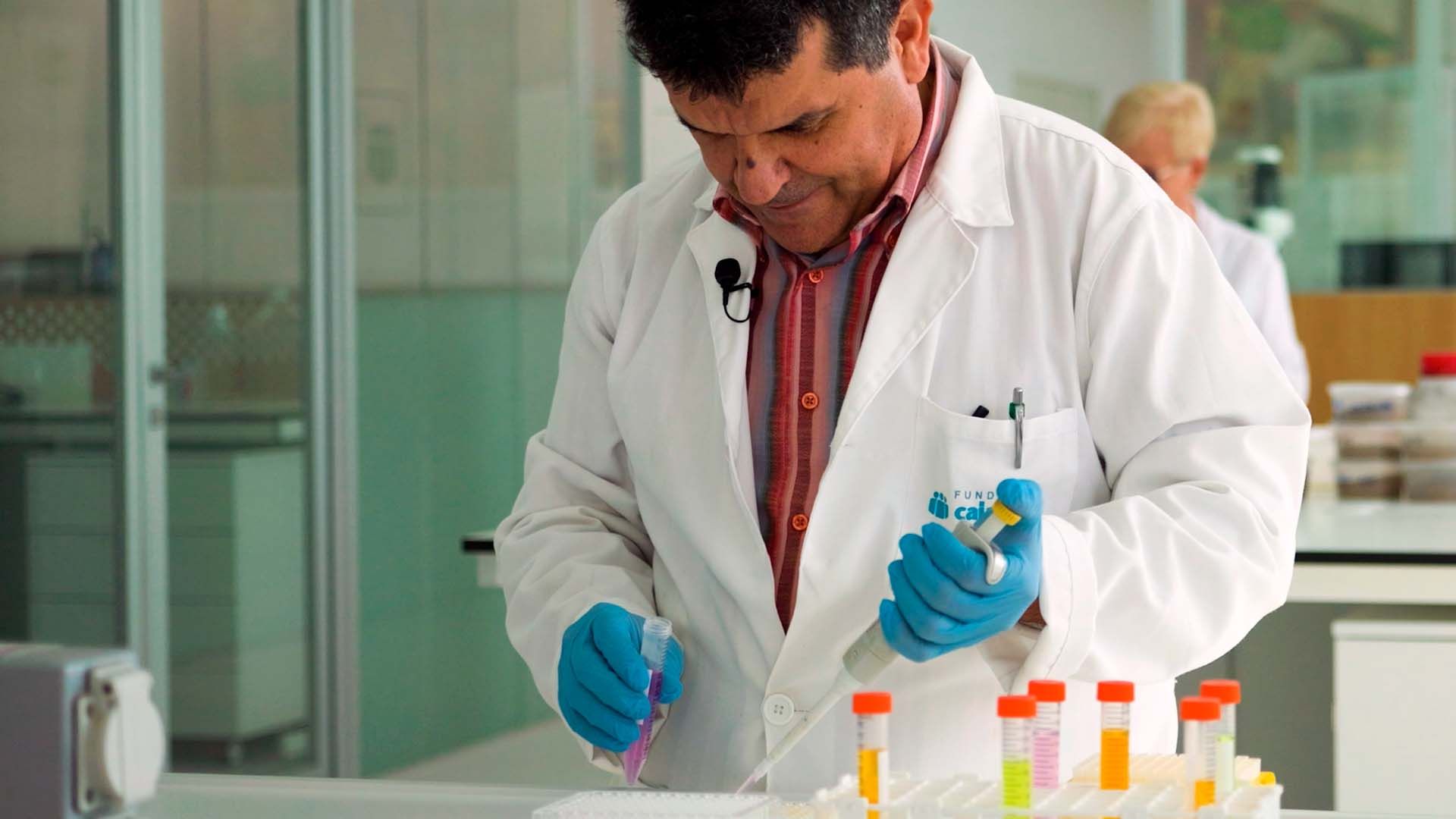 Científico con bata y guantes azules trabaja con líquidos en laboratorio.